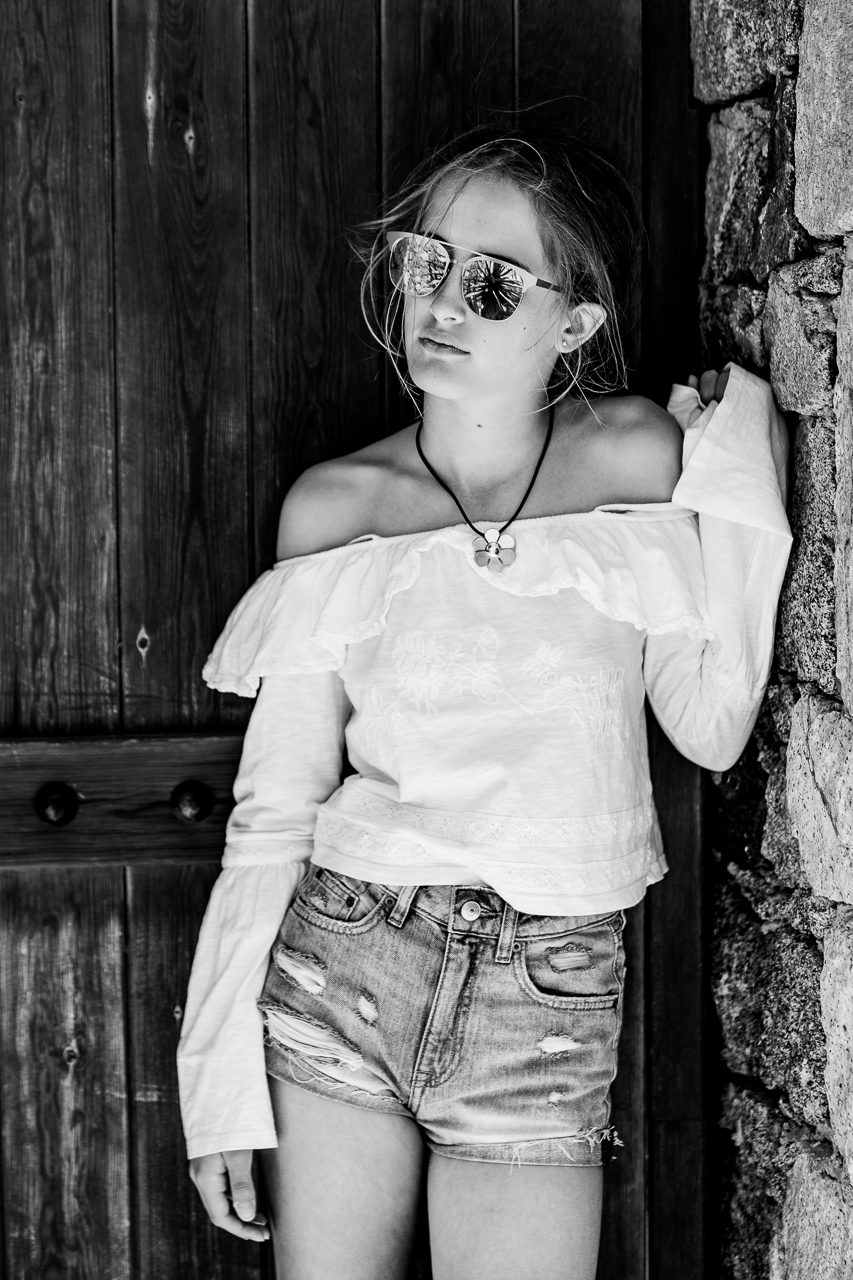 Teenage girl standing in a rustic doorway with sunglasses in back and white photograph