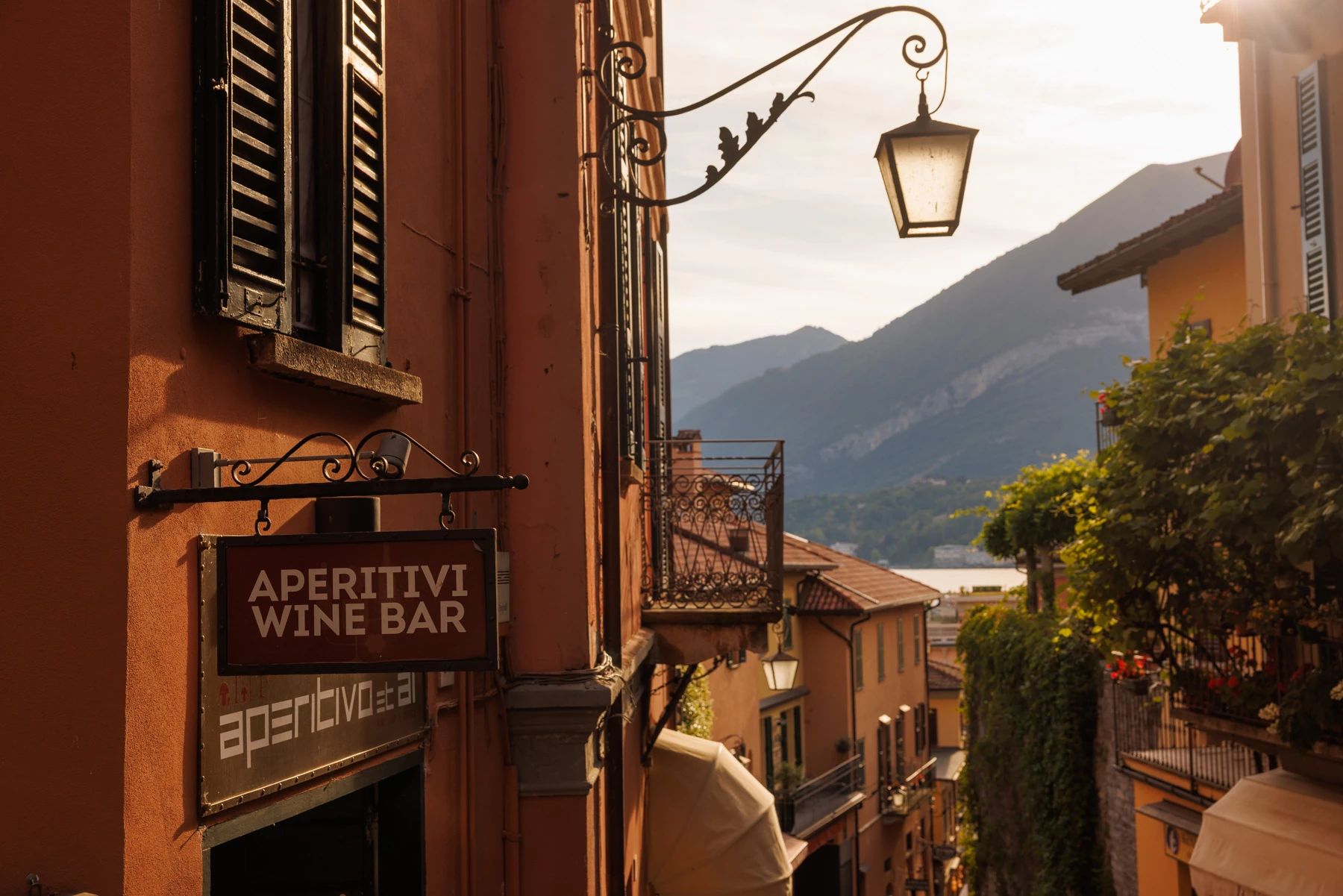 Warm evening light on a Lake Como village street, with a hanging lantern and mountains beyond.
