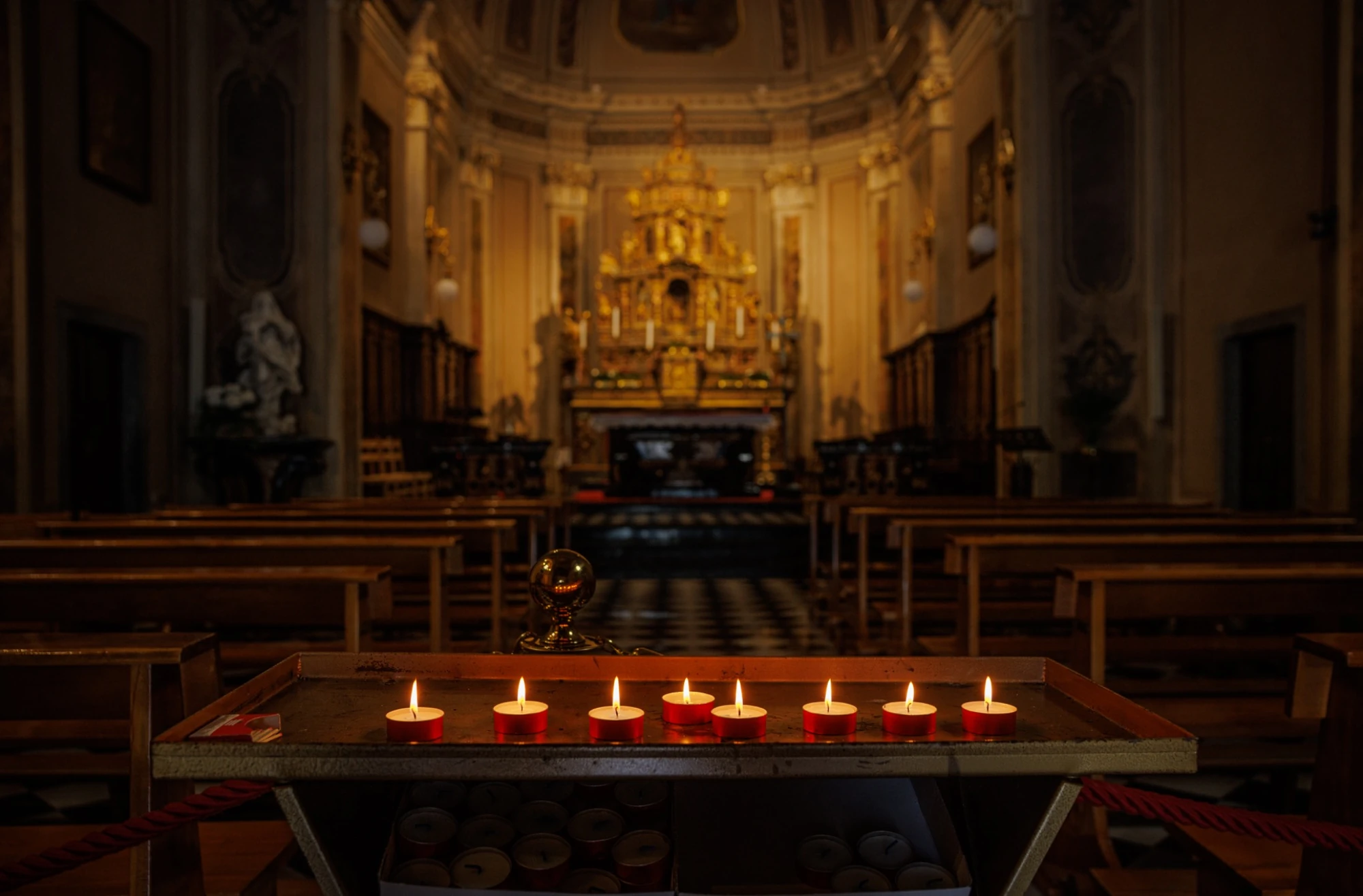Lit votive candles in the foreground of a softly illuminated church near Lake Como.