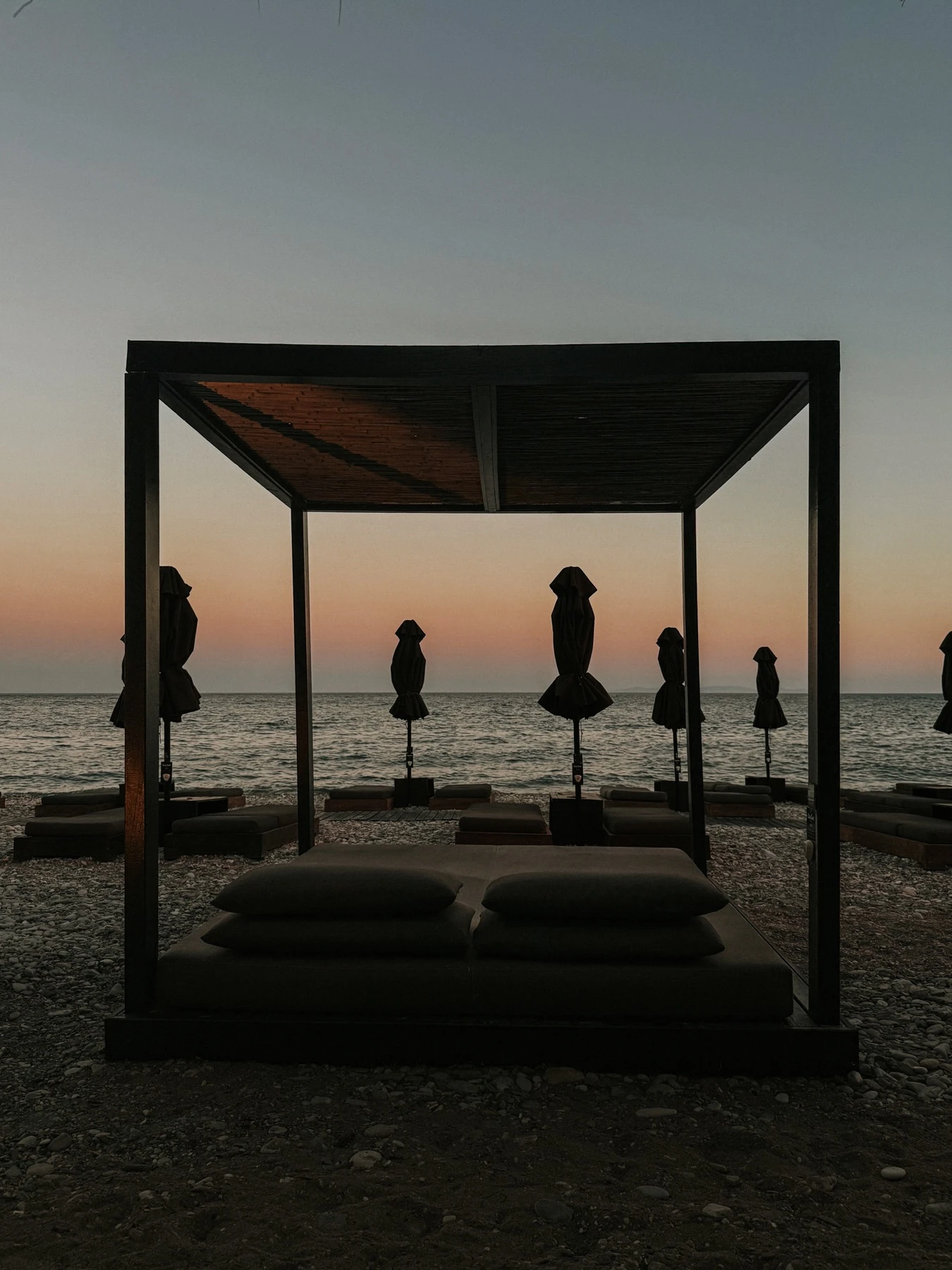 Beach cabana and closed parasols silhouetted against the evening sky over the sea in Samos.